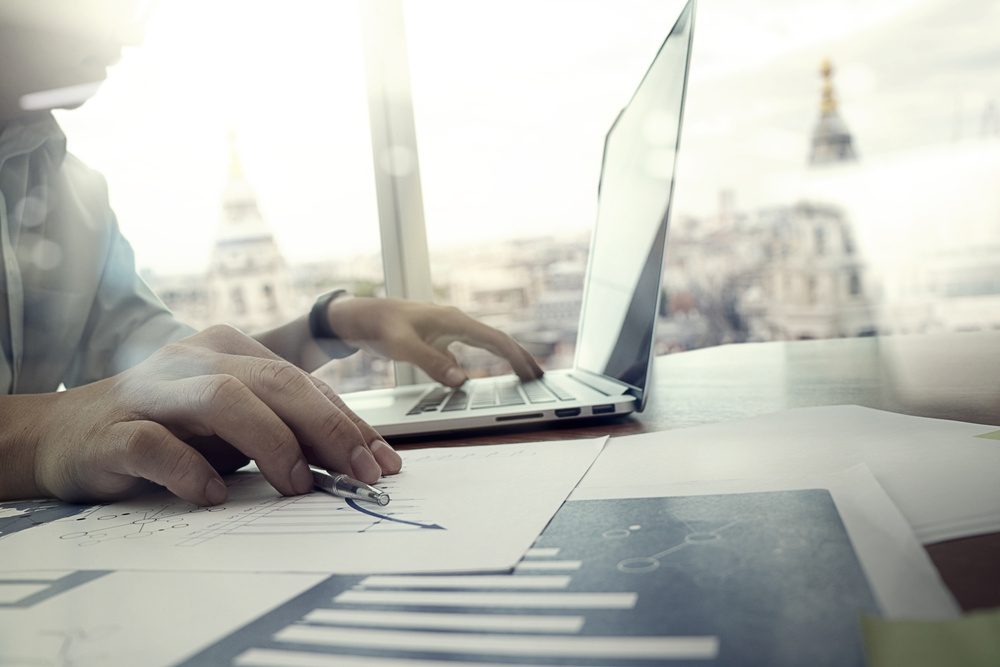 business documents on office table with laptop computer and graph financial diagram and man working in the background business documents on office table with laptop computer and graph financial diagram and man working in the background